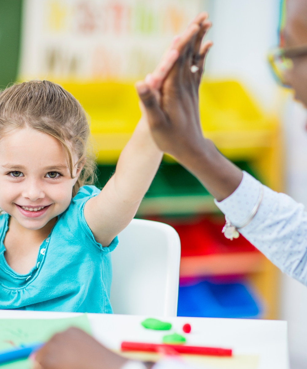 Een kind en leerkracht geven elkaar een high five, wat de samenwerking en positieve interactie in de Engelse lessen benadrukt.