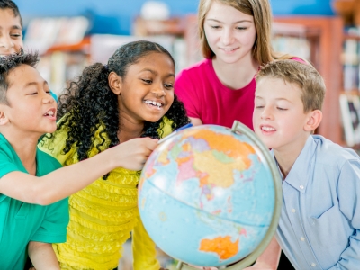 Kinderen die rondom een wereldbol staan, symboliserend voor de wereldwijde impact van samen Engels leren.